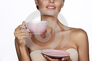 Young beautiful woman with dark hair picked up holding a ceramic cup and saucer pale pink drink tea or coffee on a white back