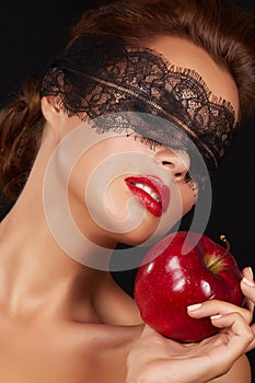 Young beautiful woman with dark lace on eyes bare shoulders and neck, holding big red apple to enjoy the taste and are dietin