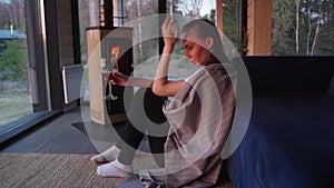 Young beautiful woman in depression, drinking alcohol, is sitting by the sofa near the fireplace in the living room