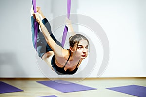 Young beautiful woman doing aerial yoga practice in purple hammock in fitness club.