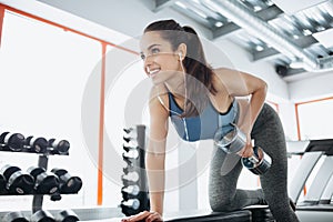 Young beautiful woman doing exercises with dumbbell in gym.