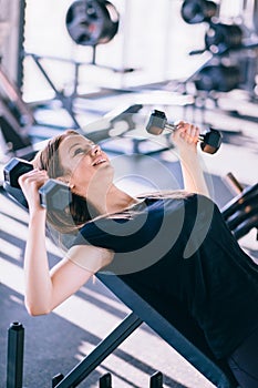 Young beautiful woman doing exercises with dumbbell in gym