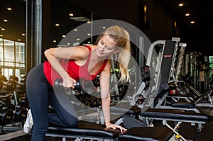 Young beautiful woman doing exercises lifting dumbbell in gym. Girl is enjoying with her training process in the morning.