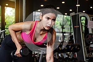 Young beautiful woman doing exercises lifting dumbbell in gym. Girl is enjoying with her training process in the morning.
