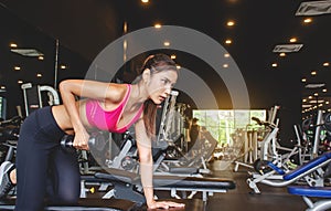 Young beautiful woman doing exercises lifting dumbbell in gym. Girl is enjoying with her training process in the morning.