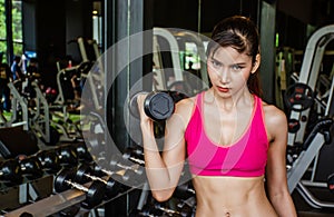 Young beautiful woman doing exercises lifting dumbbell in gym.Glad smiling girl is enjoying with her training process