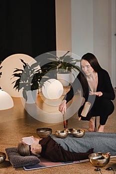 A young beautiful woman is doing a massage with singing bowls and a koshi bell to another girl. Sound therapy