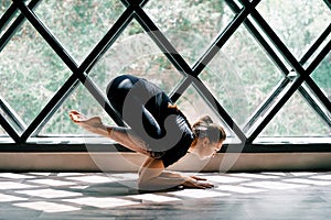 Young beautiful woman doing yoga asana baby crow pose on triangular window background