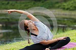 Young beautiful woman doing yoga exercise in green park. Healthy lifestyle and fitness concept.