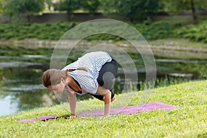 Young beautiful woman doing yoga exercise in green park. Healthy lifestyle and fitness concept.