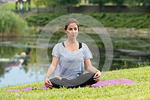 Young beautiful woman doing yoga exercise in green park. Healthy lifestyle and fitness concept.