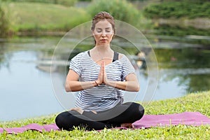 Young beautiful woman doing yoga exercise in green park. Healthy lifestyle and fitness concept.