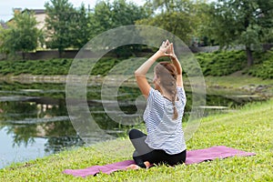 Young beautiful woman doing yoga exercise in green park. Healthy lifestyle and fitness concept.