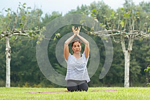 Young beautiful woman doing yoga exercise in green park. Healthy lifestyle and fitness concept.