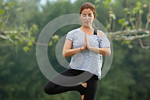 Young beautiful woman doing yoga exercise in green park. Healthy lifestyle and fitness concept.