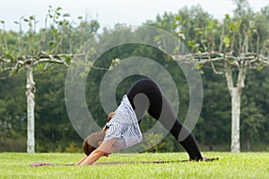 Young beautiful woman doing yoga exercise in green park. Healthy lifestyle and fitness concept.