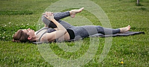 Young beautiful woman doing yoga exercise in green park near the pond. Exercices for improve the flexibility. Wellbeing