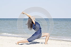 Young beautiful woman doing yoga at seaside in blue dress