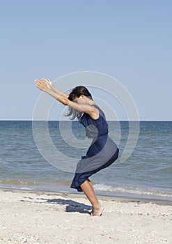 Young beautiful woman doing yoga at seaside in blue dress