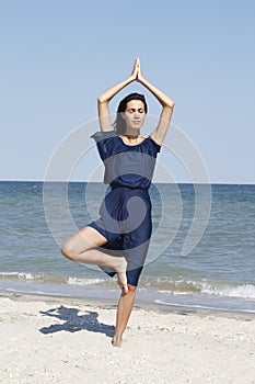 Young beautiful woman doing yoga at seaside in blue dress