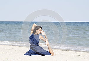 Young beautiful woman doing yoga at seaside in blue dress