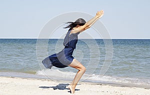 Young beautiful woman doing yoga at seaside in blue dress