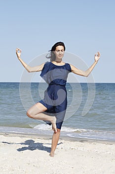 Young beautiful woman doing yoga at seaside in blue dress