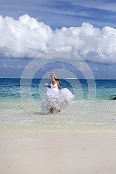 Young beautiful woman in a dress of the bride runs on waves of the sea