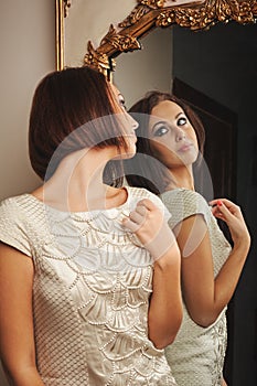 Young beautiful woman in a dress looks in an old mirror