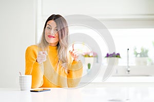 Young beautiful woman drinking a cup of coffee at home pointing fingers to camera with happy and funny face