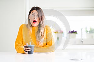 Young beautiful woman drinking a cup of coffee at home scared in shock with a surprise face, afraid and excited with fear