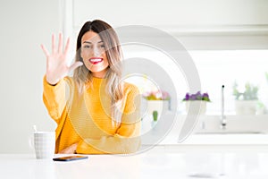 Young beautiful woman drinking a cup of coffee at home showing and pointing up with fingers number five while smiling confident