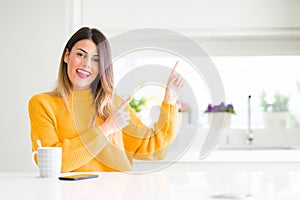 Young beautiful woman drinking a cup of coffee at home smiling and looking at the camera pointing with two hands and fingers to