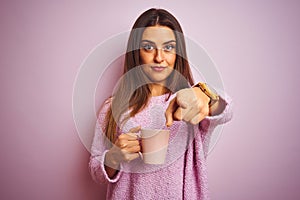 Young beautiful woman drinking cup of coffee standing over isolated pink background pointing with finger to the camera and to you,