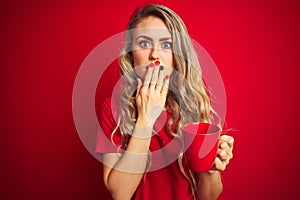 Young beautiful woman drinking a cup of cooffe over red isolated background cover mouth with hand shocked with shame for mistake, photo