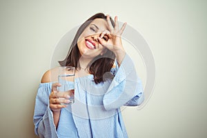 Young beautiful woman drinking a glass of fresh water over isolated background with happy face smiling doing ok sign with hand on