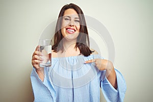 Young beautiful woman drinking a glass of fresh water over isolated background with surprise face pointing finger to himself