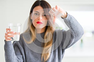 Young beautiful woman drinking glass of water at home with angry face, negative sign showing dislike with thumbs down, rejection