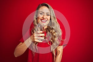 Young beautiful woman drinking a glass of water over red isolated background with a happy face standing and smiling with a