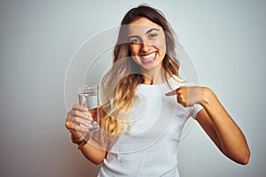 Young beautiful woman drinking a glass of water over white  background with surprise face pointing finger to himself