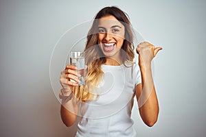 Young beautiful woman drinking a glass of water over white isolated background pointing and showing with thumb up to the side with