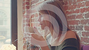 Young beautiful woman drinking hot coffee in cafe. Happy relaxed girl enjoying cup of warm steaming beverage.