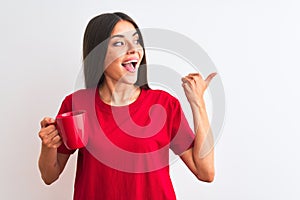 Young beautiful woman drinking red cup of coffee standing over isolated white background pointing and showing with thumb up to the