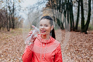 Young beautiful woman drinking water during morning jogging in the autumn park