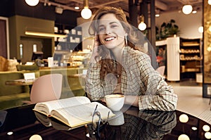 Young beautiful woman drinks coffee and reading book in cafe