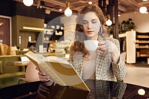 Young beautiful woman drinks coffee and reading book in cafe