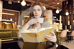 Young beautiful woman drinks coffee and reading book in cafe