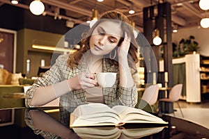 Young beautiful woman drinks coffee and reading book in cafe