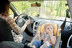 Young beautiful woman driving a car. On a front seat mounted child safety seat with a pretty 1 year old toddler boy. Child