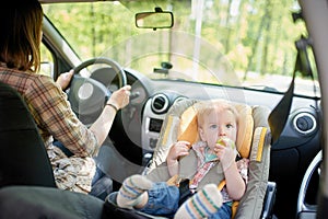 Young beautiful woman driving a car. On a front seat mounted child safety seat with a pretty 1 year old toddler boy. Child